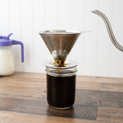 Stainless steel pour-over coffee filter resting on a Mason jar filled with brewed coffee.