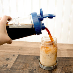 Deep Blue Regular Mouth Pour & Store shaker lid with carry loop, used to pour a drink from a Mason jar into an ice-filled Mason jar.