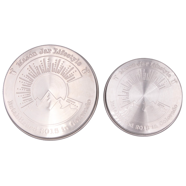 Two stainless steel storage lids for Mason jars up close, showing off the design that says "Mason Jar Lifestyle" and "Established 2015 in Colorado" with a big "C" in the middle with a silhouette of a mountain, a sun, and sun rays.