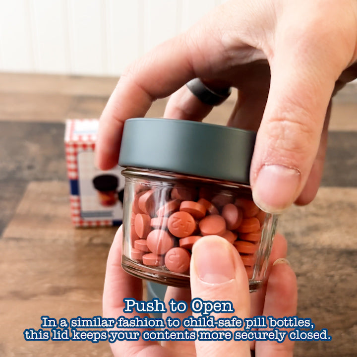 Demonstrates the function of the lid, showing that it works similar to a child safe lid on a pill container: needing to be pressed down and turned to open the container.